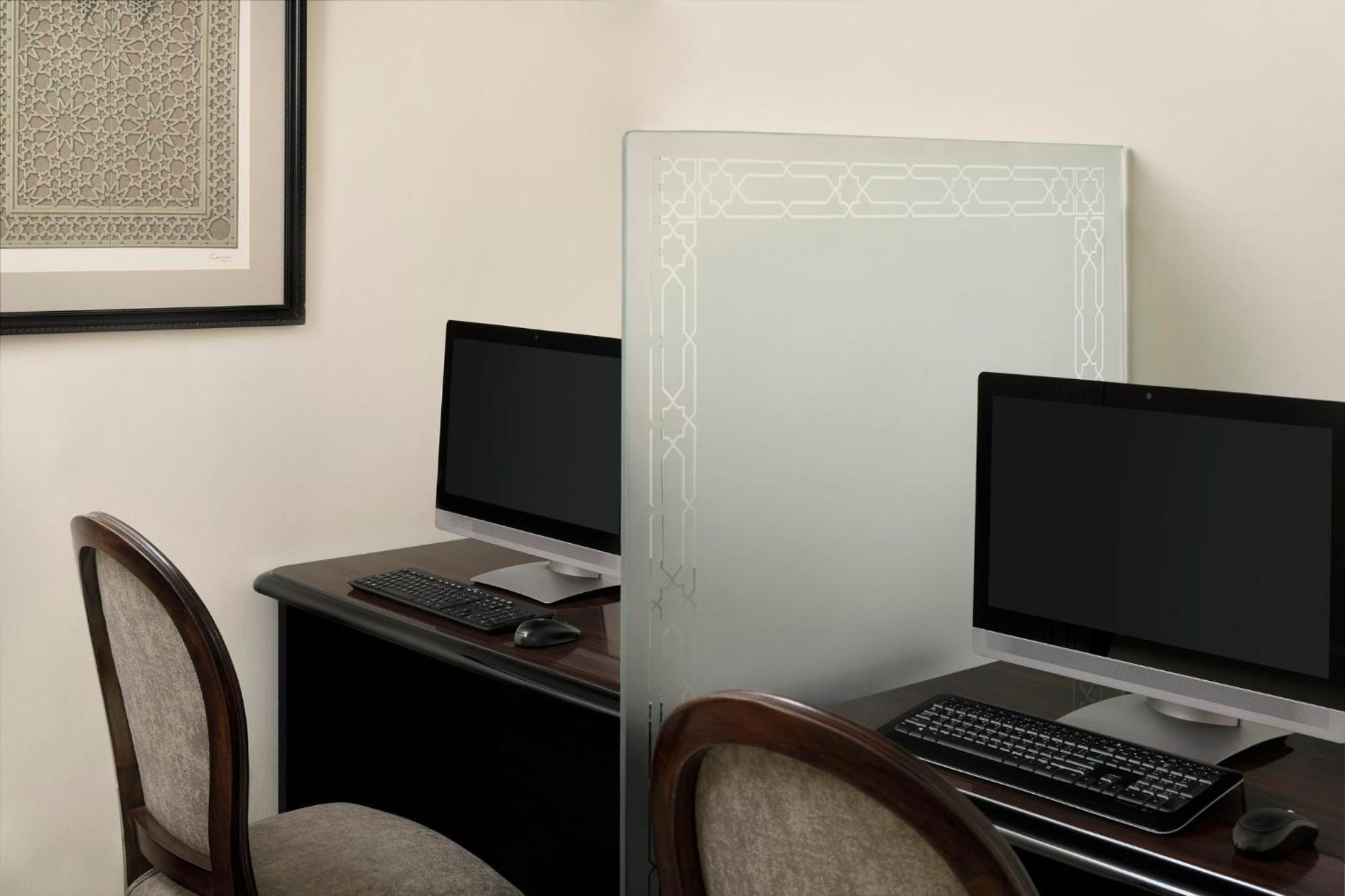 Intercontinental Dar Al Iman Madinah By Ihg Hotel Medina Exterior foto The photo shows a small office or workspace area featuring two computer stations. Each station has a black monitor, a keyboard, and appears to be set up on a dark wooden desk. A translucent glass partition is placed between the two workstations, prov