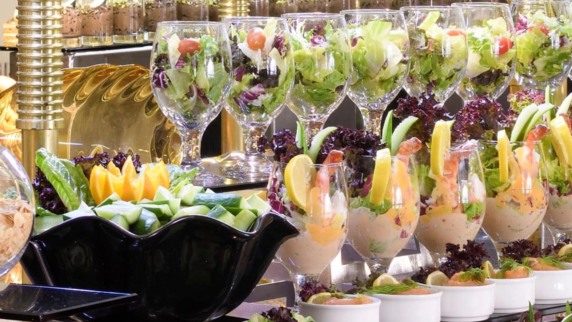 Intercontinental Dar Al Iman Madinah By Ihg Hotel Medina Exterior foto The photo features an elegant display of food items. In the background, there are several clear glasses filled with vibrant salads, featuring various types of greens and garnishes. In the foreground, there is a decorative black bowl containing cut pi