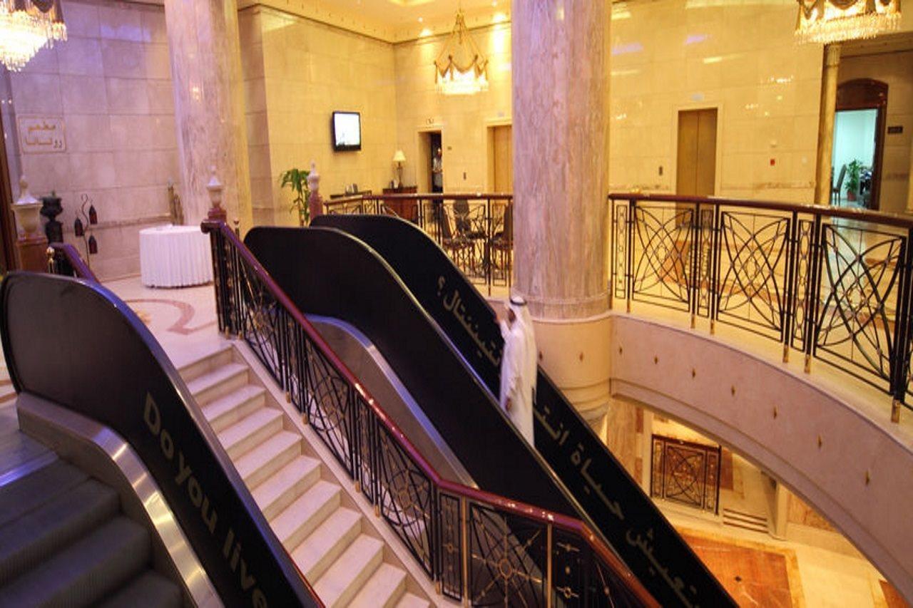 Intercontinental Dar Al Iman Madinah By Ihg Hotel Medina Interior foto The photo depicts an elegant interior space, likely within a hotel or a large building. There is a grand staircase visible, which features a combination of stairs and escalators. The design includes decorative railings and marble pillars, contributin